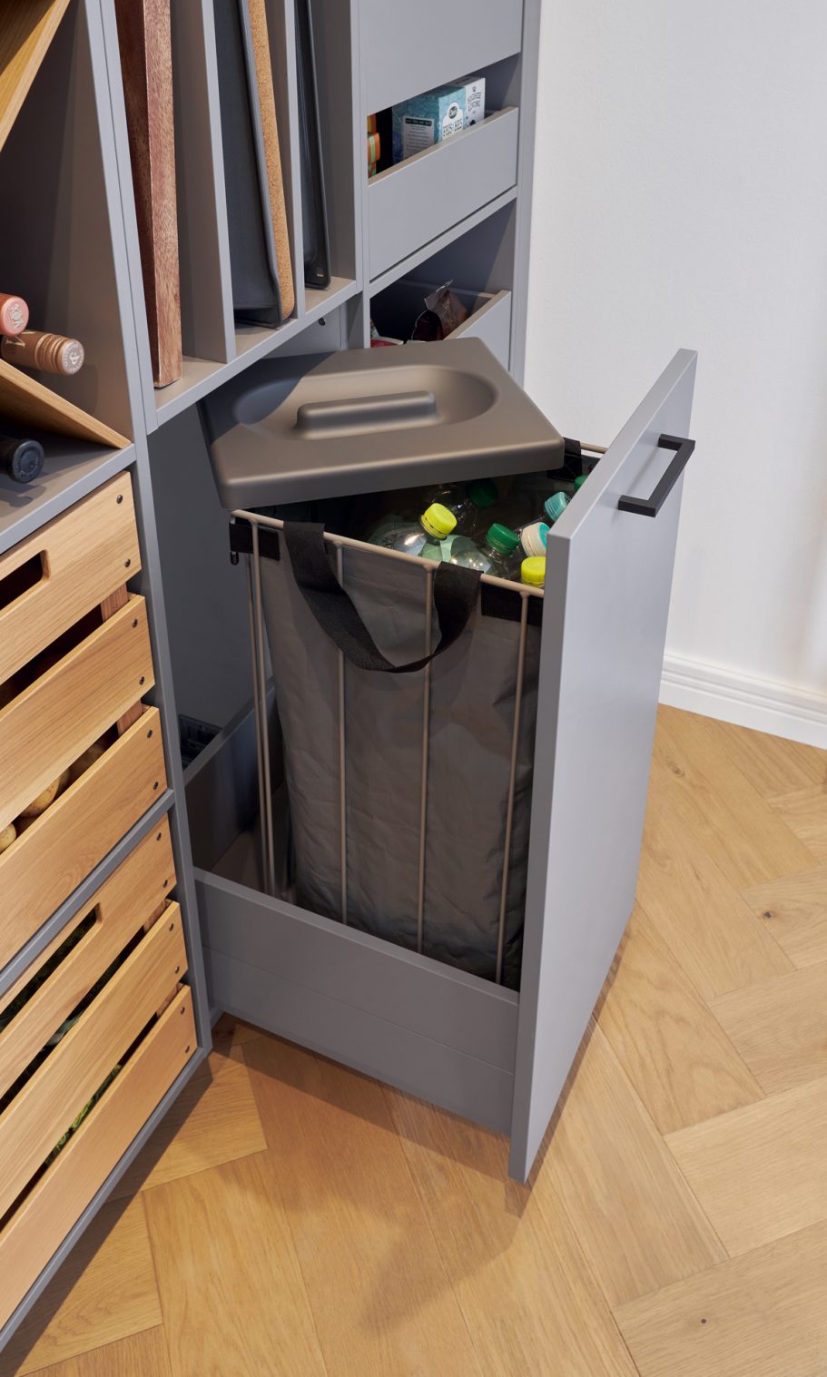 Grauener Abfallbehälter in einem offenen Schrank mit verschiedenen Fächern.