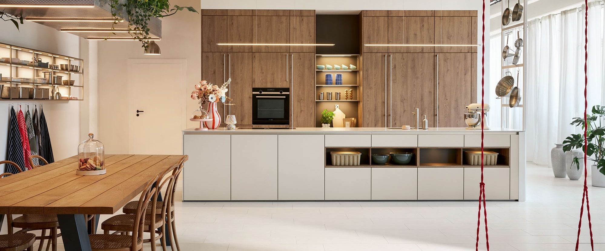 Küchenzeile in Holzoptik mit sandfarbener Insel. Davor steht ein Holztisch mit Stühlen.