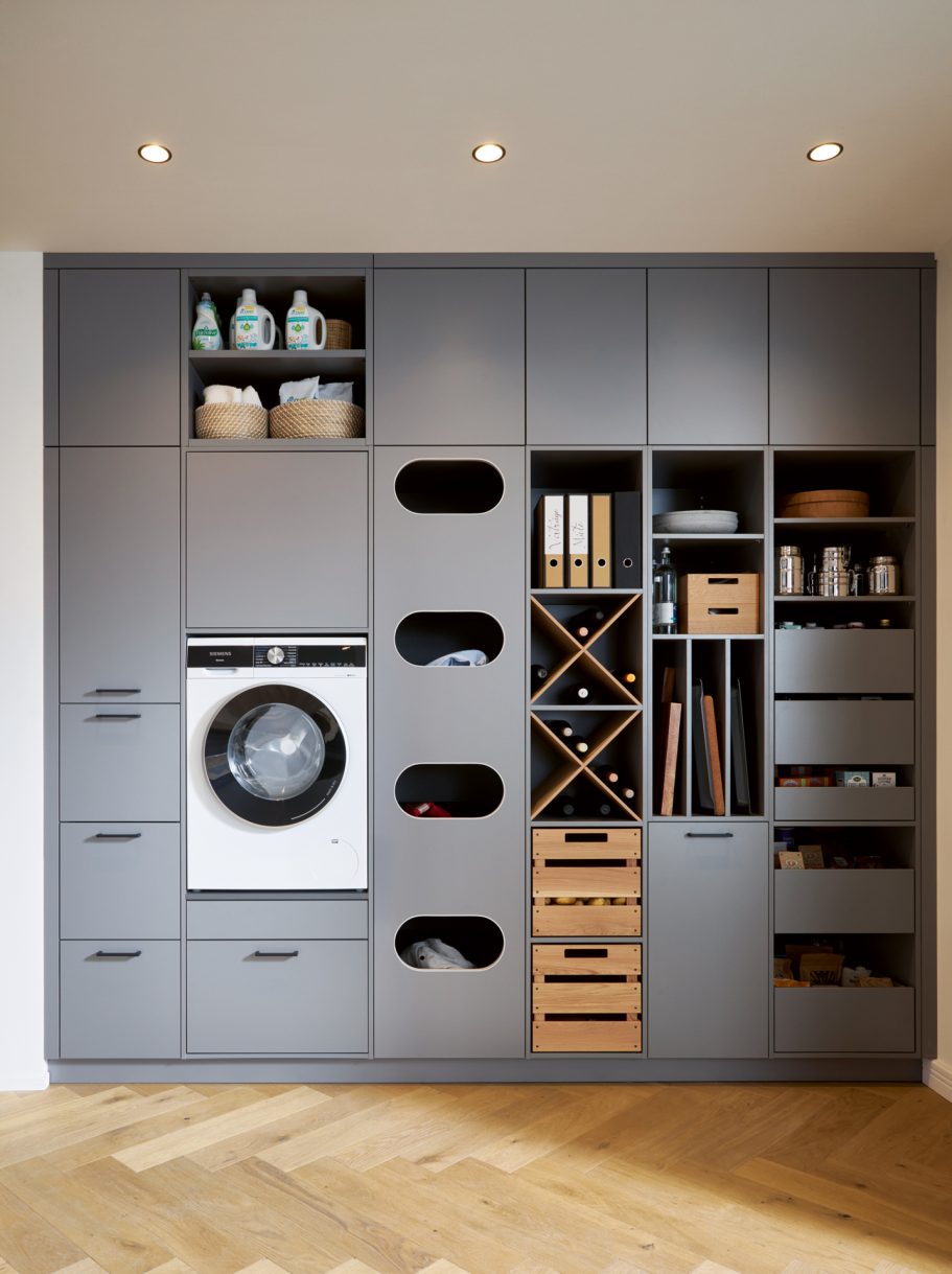 Moderne graue Wand mit Waschmaschine, Regalen und organisierten Aufbewahrungskästen.